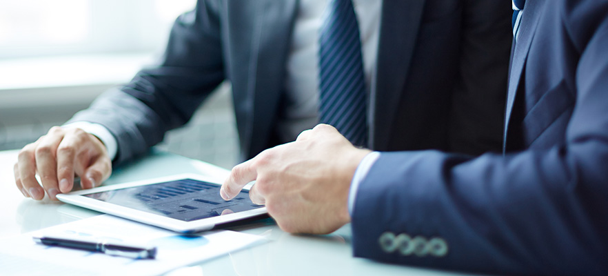 Two businessmen sitting at a table using a digital tablet.