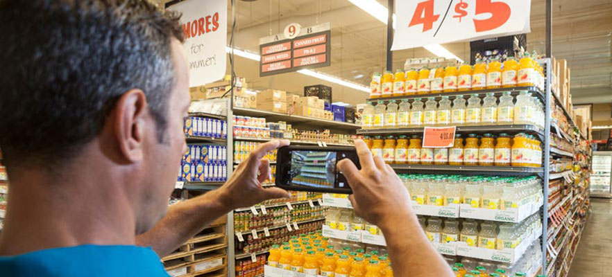 A man taking a picture of a grocery store product display using his mobile device.